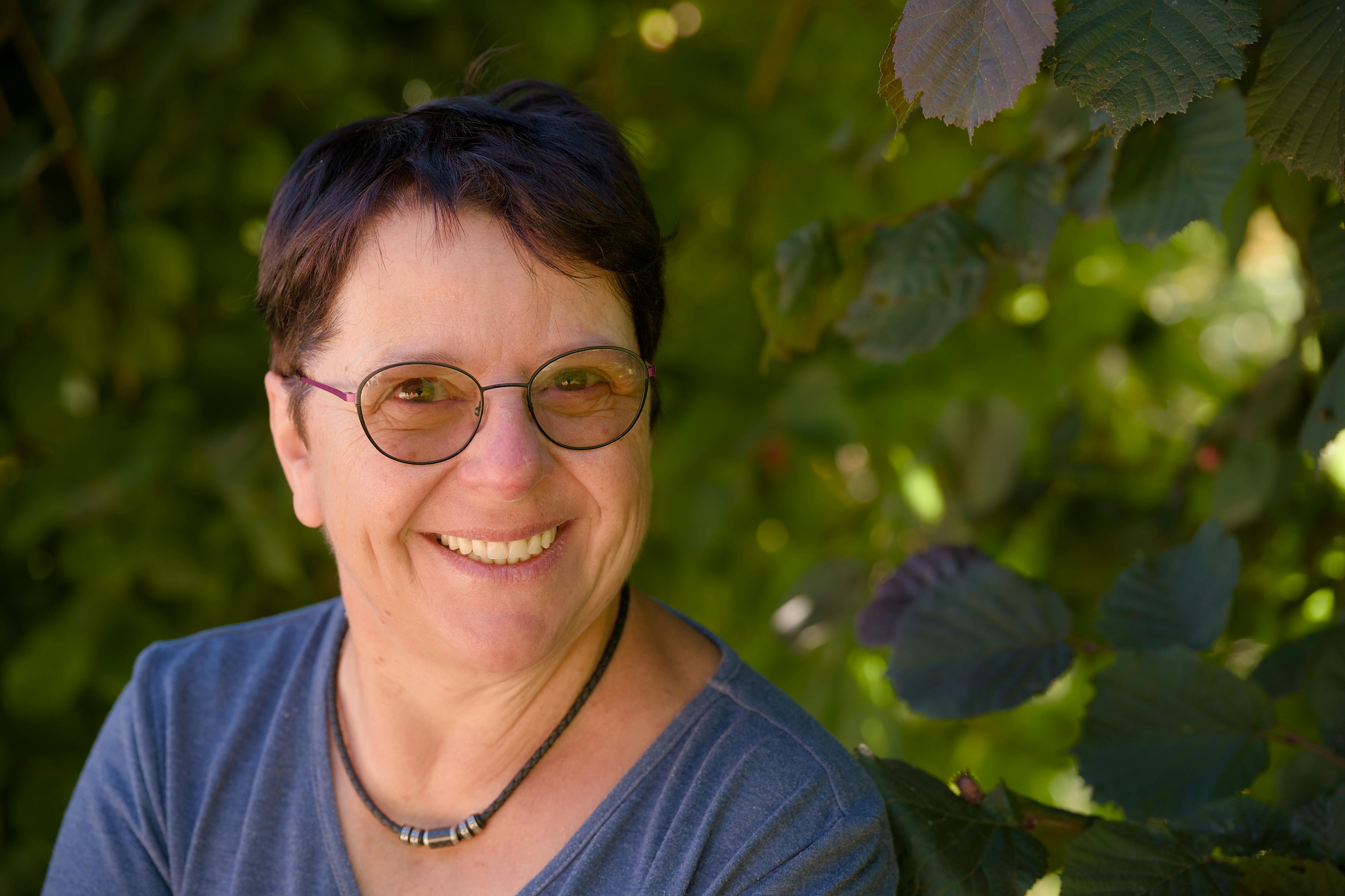 Portrait of a cheerful woman wearing eyeglasses, smiling amidst summer foliage.
