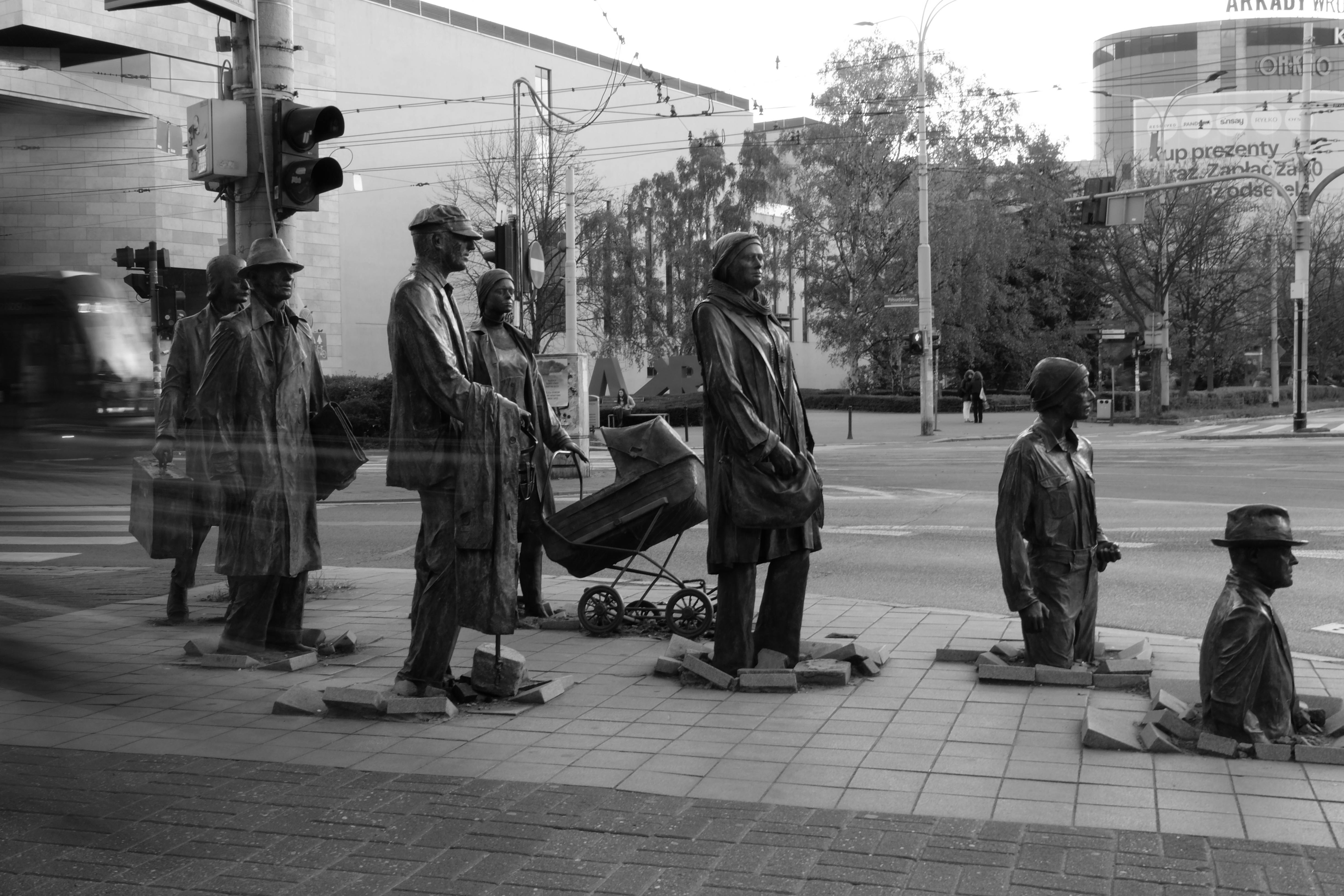 Black and white photo of life-sized human statues at a Wroclaw street intersection, depicting daily life.