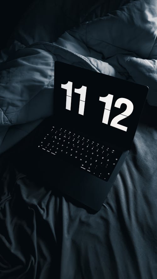 Free A Laptop Standing on a Bed Displaying the Time Stock Photo