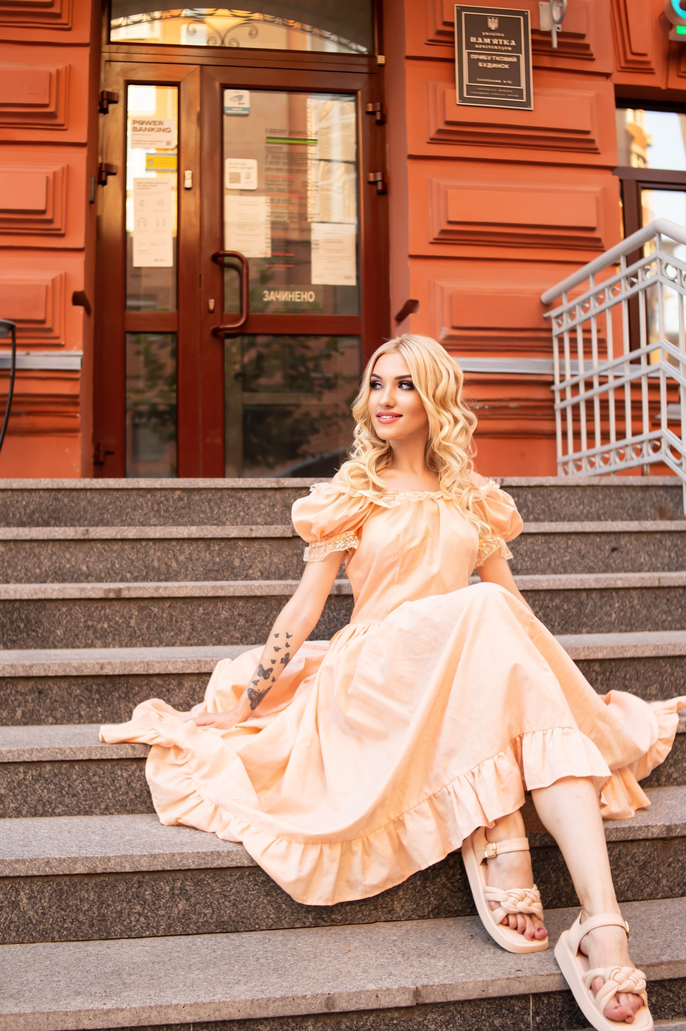 A blonde woman in a peach dress sitting on steps · Free Stock Photo