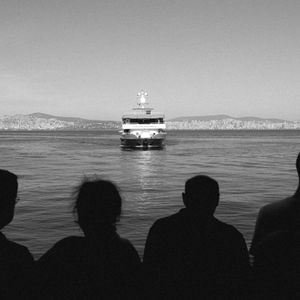 Silhouetted commuters watching a ferry cross the water — photo by Burak Argun on Pexels