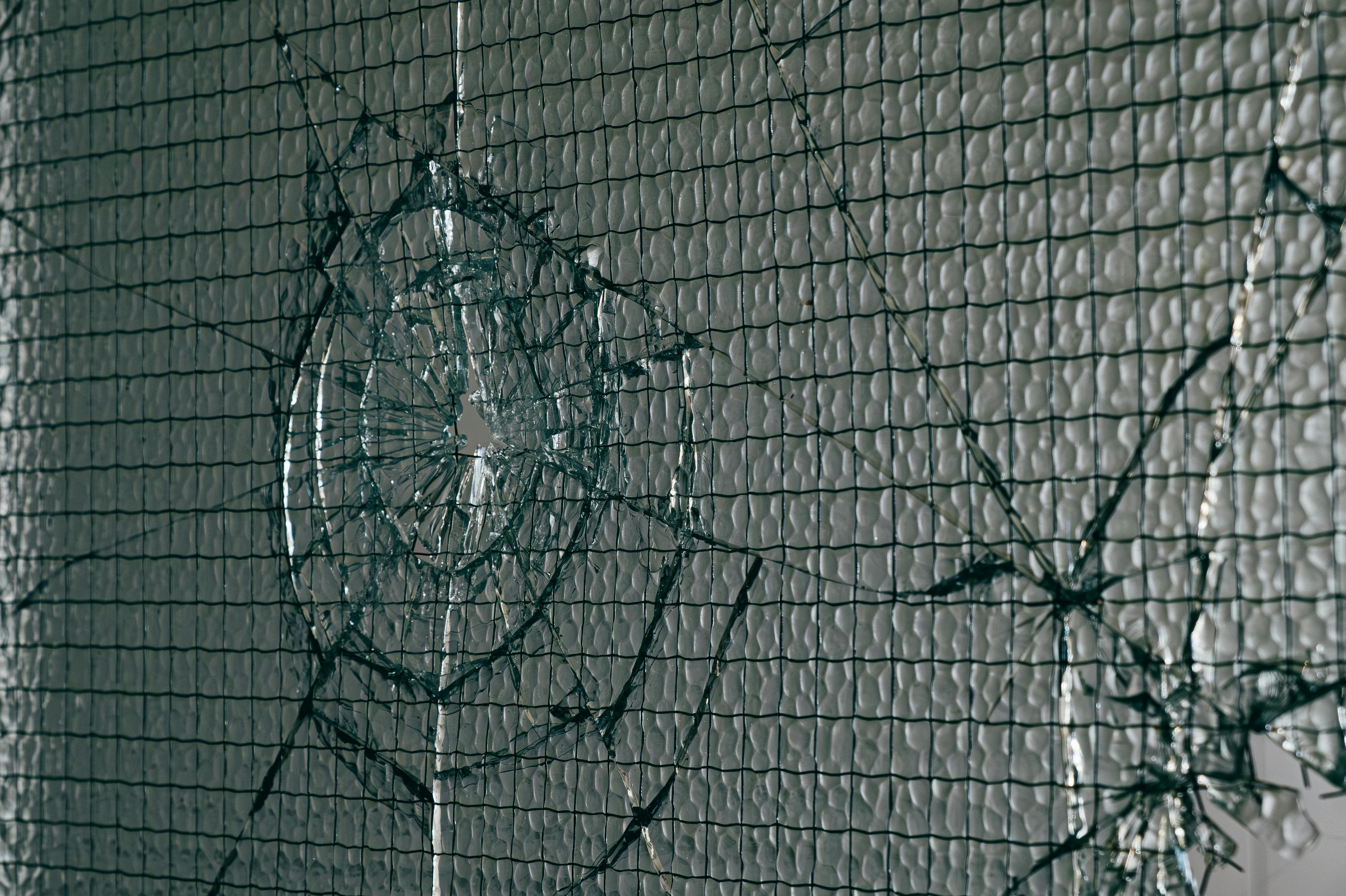 Close-up view of a shattered safety glass window with intricate wire patterns and light reflections.