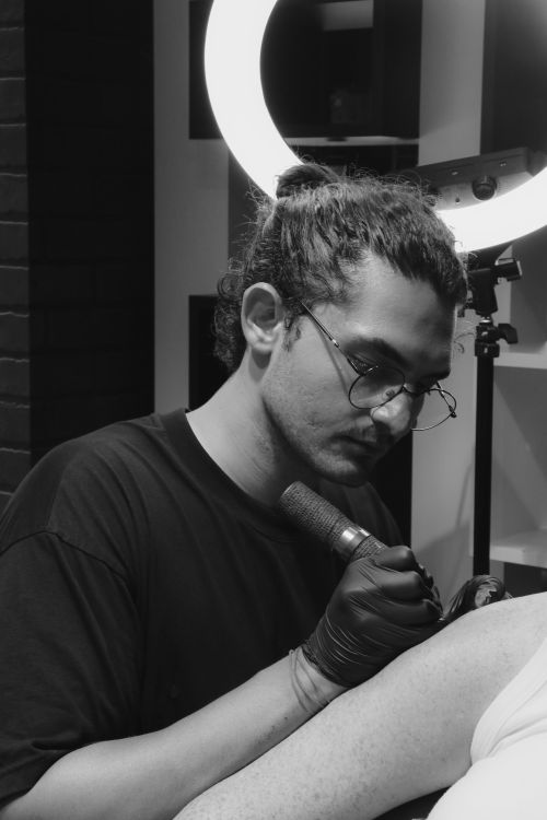 Free Tattoo artist focused on working in a studio, using a tattoo machine in monochrome. Stock Photo