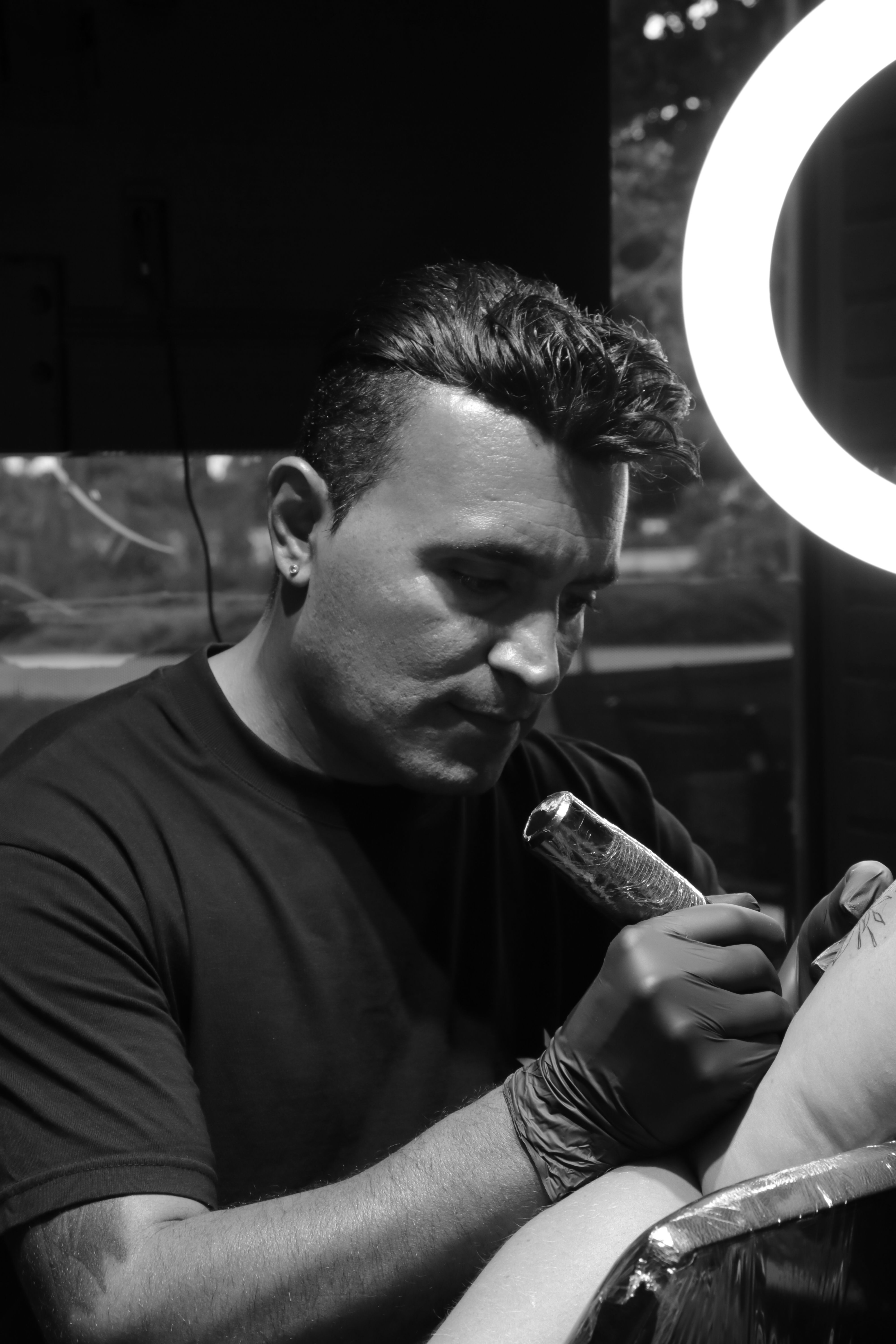 Black and white image of a tattoo artist focused on his craft in a studio.