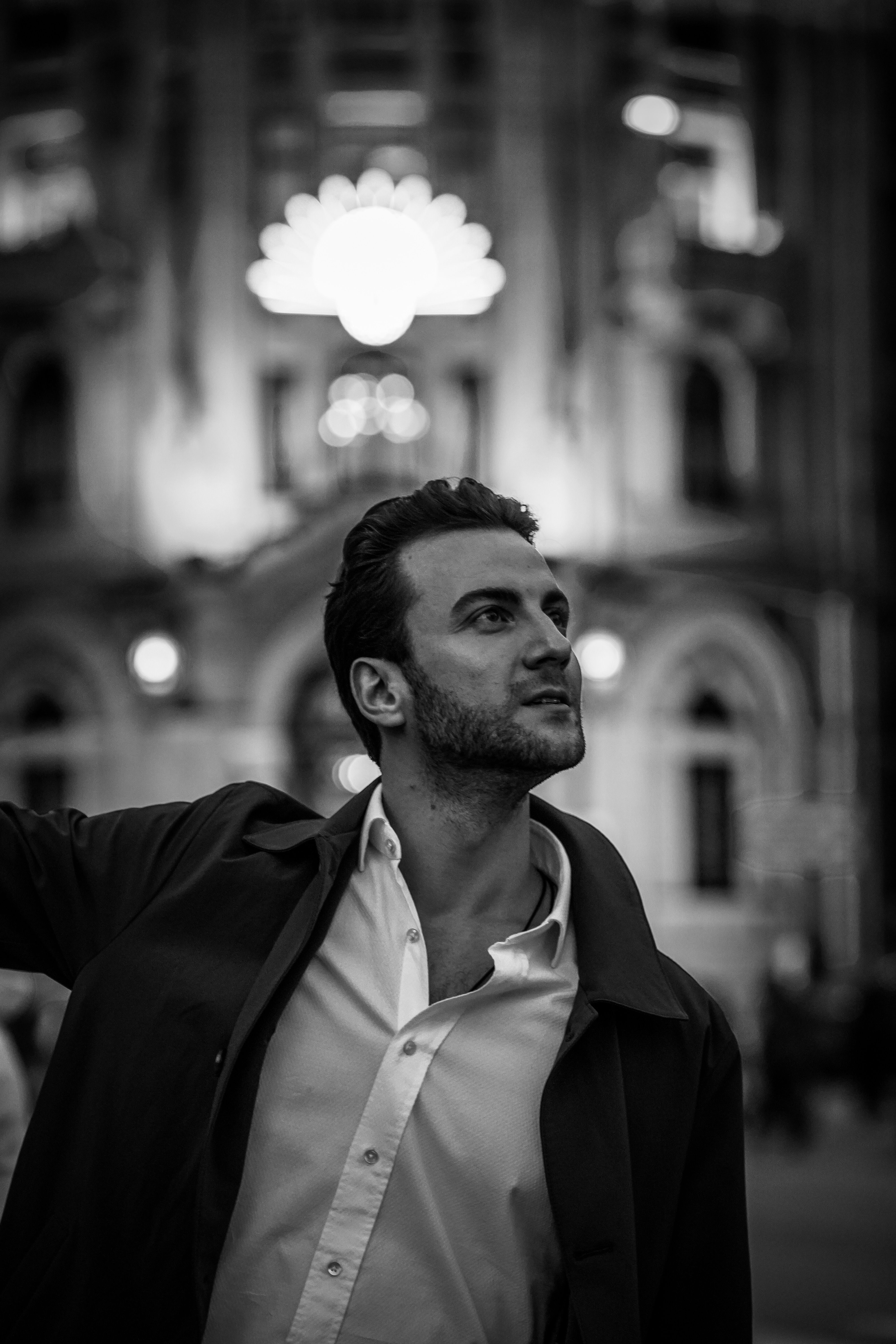 Black and white shot of a stylish man standing against the backdrop of Ankara's urban architecture at night.