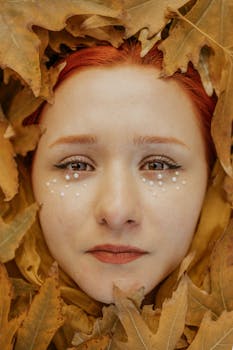 A portrait of a woman with red hair surrounded by autumn leaves, emphasizing fall aesthetics and artistic makeup.