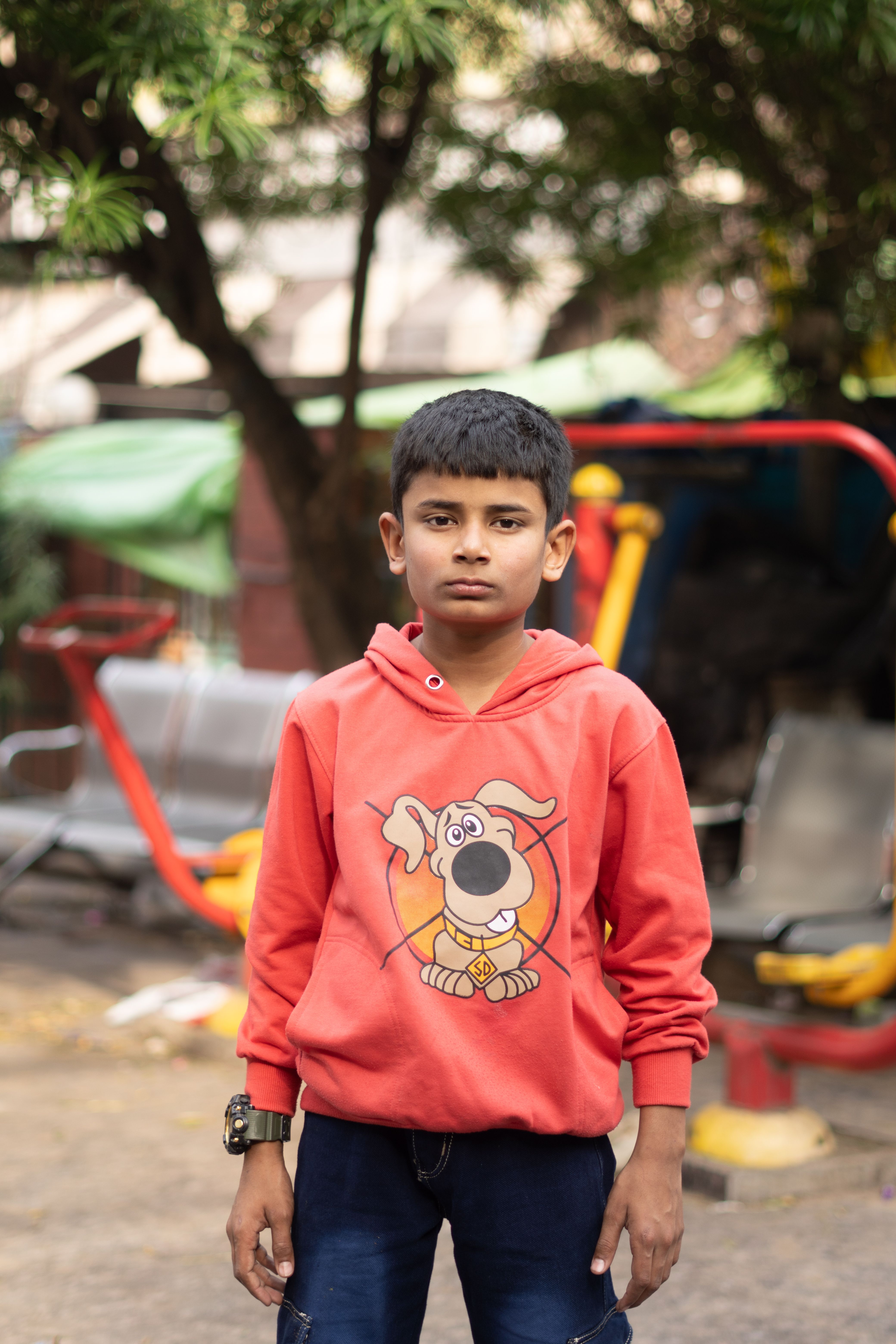 Portrait of a boy in a red hoodie standing outdoors in a playground in Jammu.