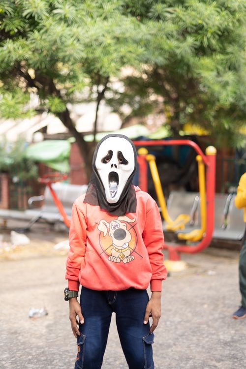Free Teenager wearing Scream mask in Jammu park, expressing urban youth culture. Stock Photo