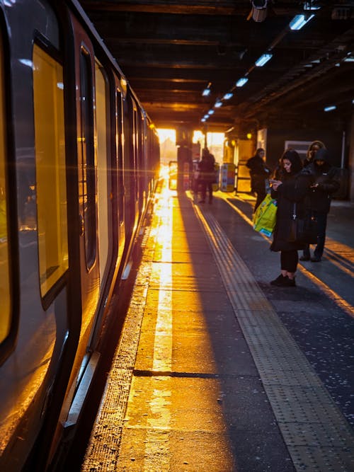 Sun Shining between the Train and People Standing on a Railway Station Platform 