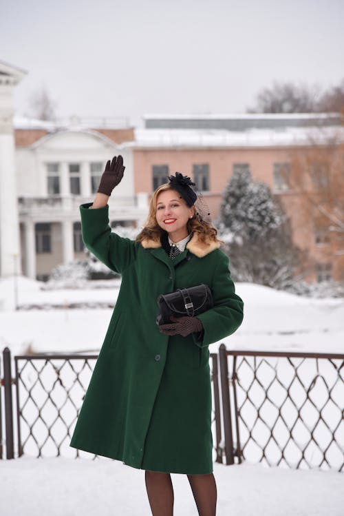 Free Smiling Woman in Green Coat Standing with Arm Raised Stock Photo