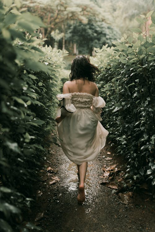 Back View of a Woman in a Dress Running Barefoot through a Park in Rain 