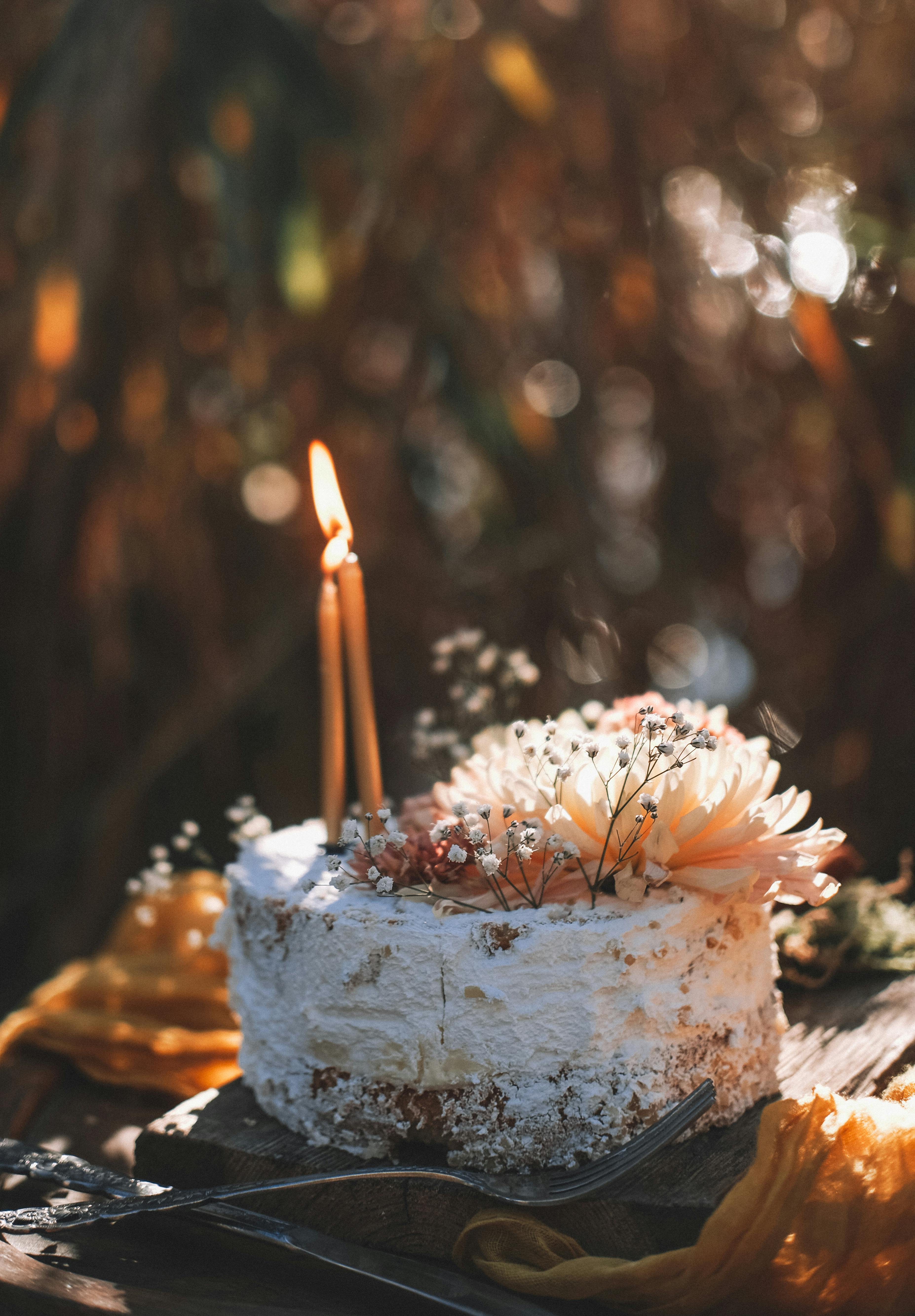Rustic cake adorned with flowers and lit candles, captured in soft natural light.