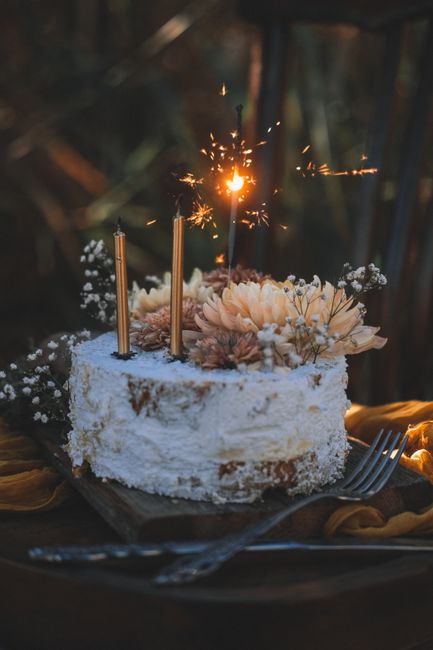 A rustic cake adorned with flowers and candles in a dimly lit, cozy setting. Perfect for celebrations.