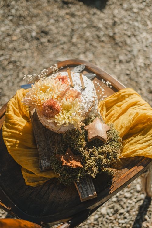Free Artistic floral-topped cake with candles and moss on a rustic board outdoors. Stock Photo