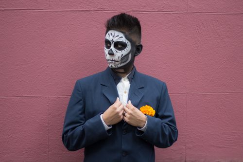 Free Man in suit with Day of the Dead skull makeup posing with a marigold on pink wall. Stock Photo