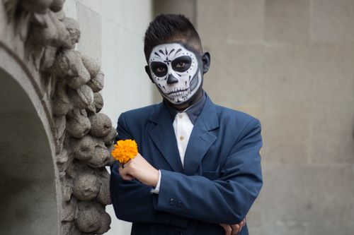 Free Man dressed in a suit with sugar skull makeup holding a marigold flower, celebrating Dia de los Muertos. Stock Photo
