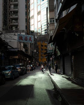 Moody urban street in Hong Kong with buildings and people at dusk, showcasing city life.