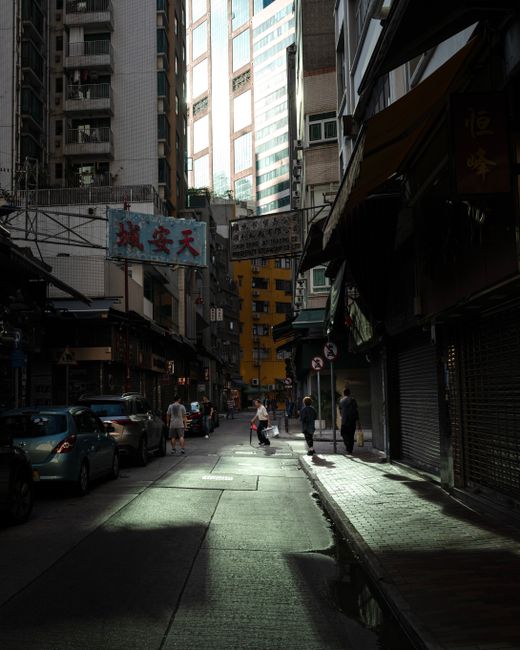 Moody urban street in Hong Kong with buildings and people at dusk, showcasing city life.