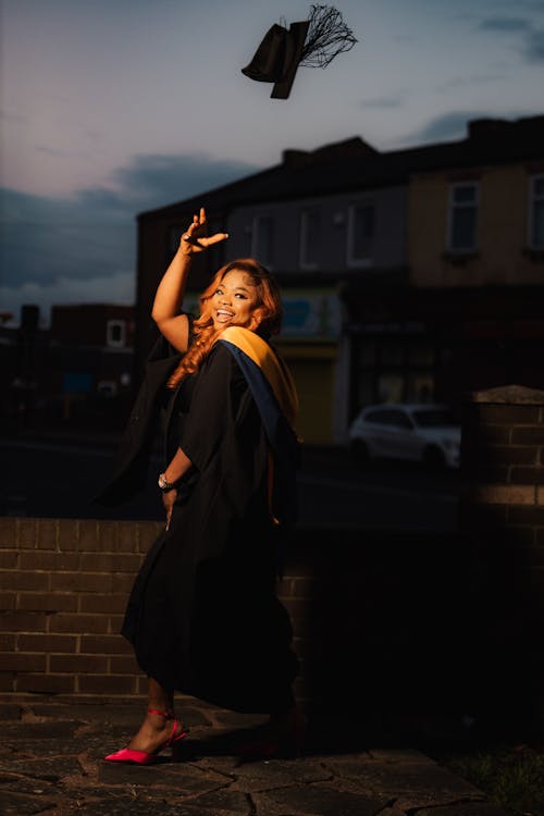 Evening Photograph of a Woman Wearing a Graduation Gown Throwing a Hat into the Sky