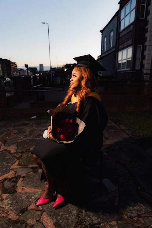 Graduation Student Sitting Outdoors at Dusk with a Bouquet