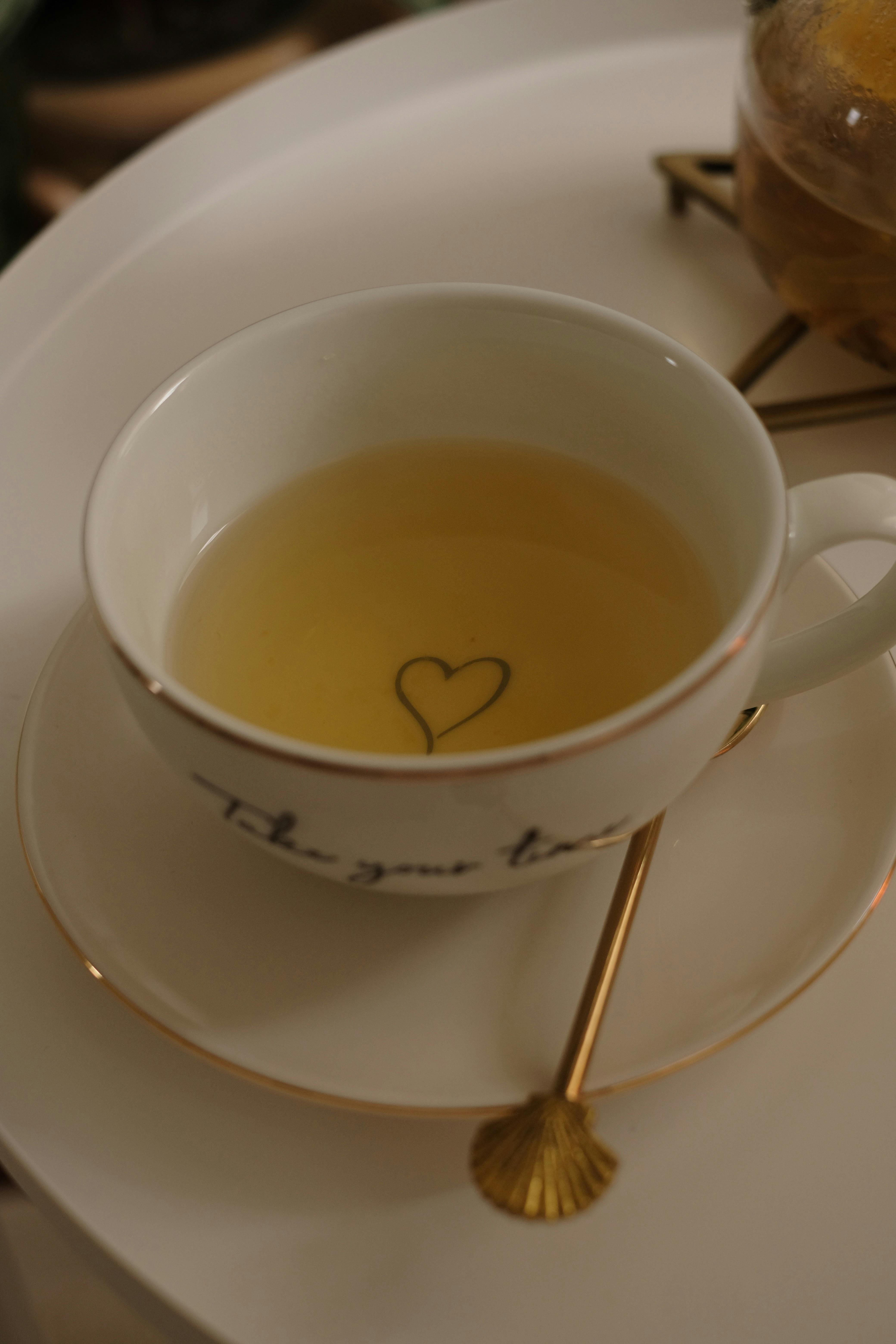 A close-up of a porcelain tea cup with a heart detail on a golden spoon and tray.