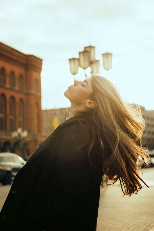 Free Fashionable woman poses outdoors with sunlit hair in urban setting. Stock Photo
