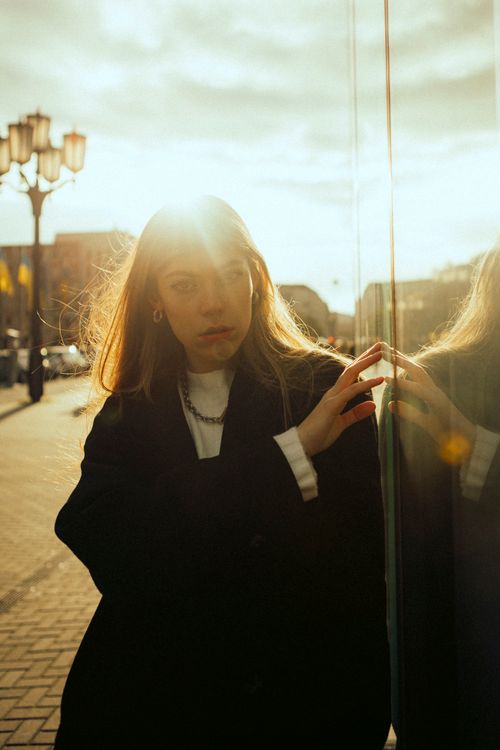 Free Dramatic portrait of a woman in a coat with sunlight reflection on glass, urban setting. Stock Photo