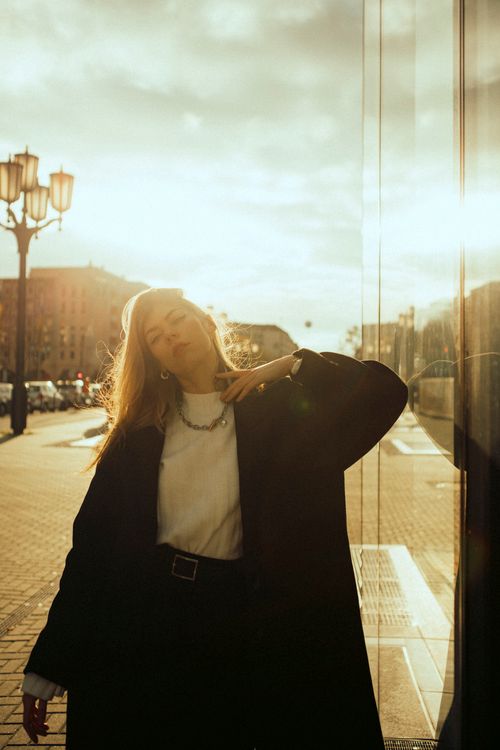 Free Stylish woman in a coat poses against a cityscape backdrop during sunset. Stock Photo