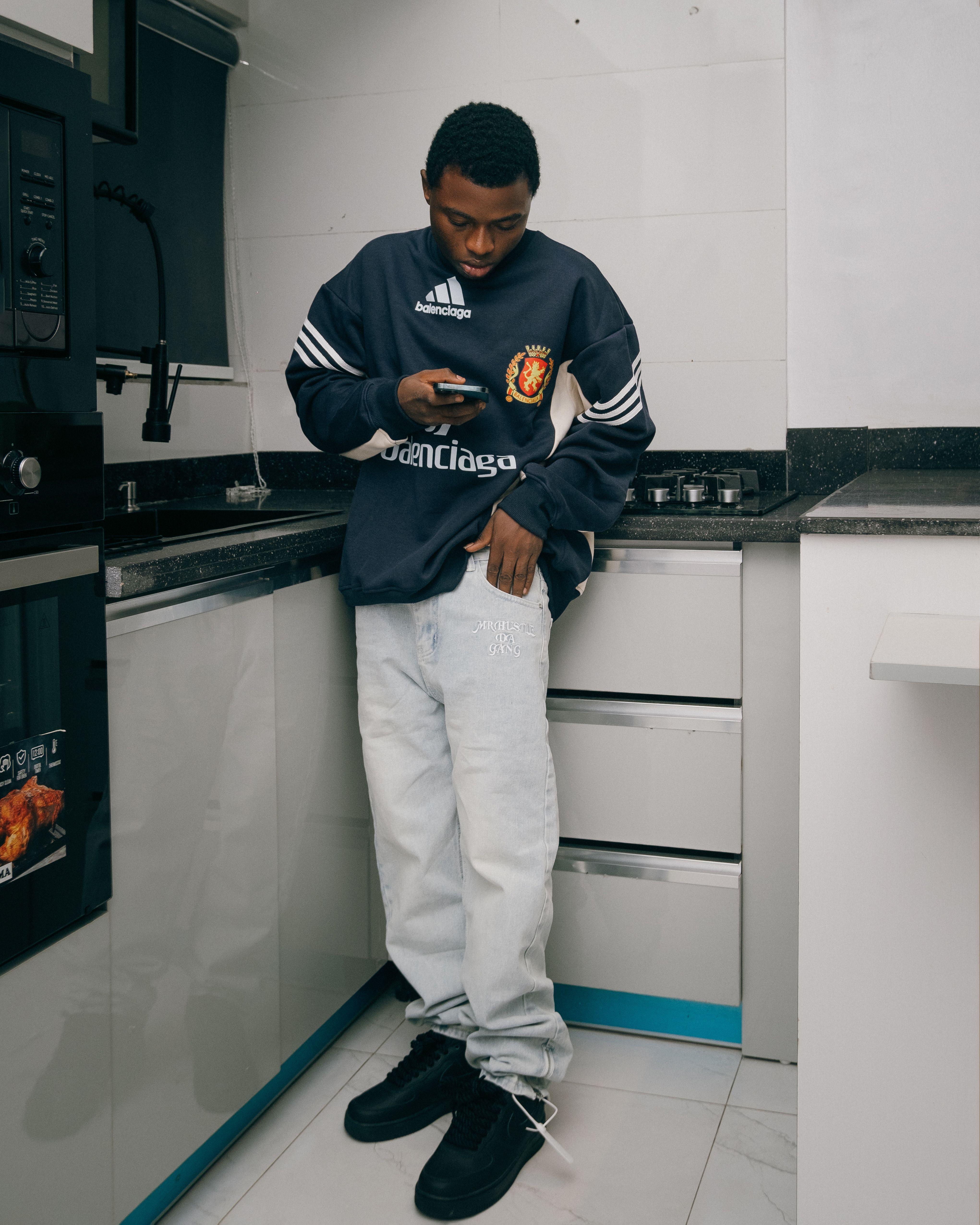 Man casually using a smartphone while leaning on kitchen counter. Relaxed indoor scene.
