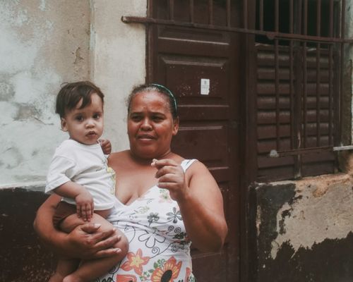 Free Woman holding a baby outside an aged urban building, depicting everyday life. Stock Photo