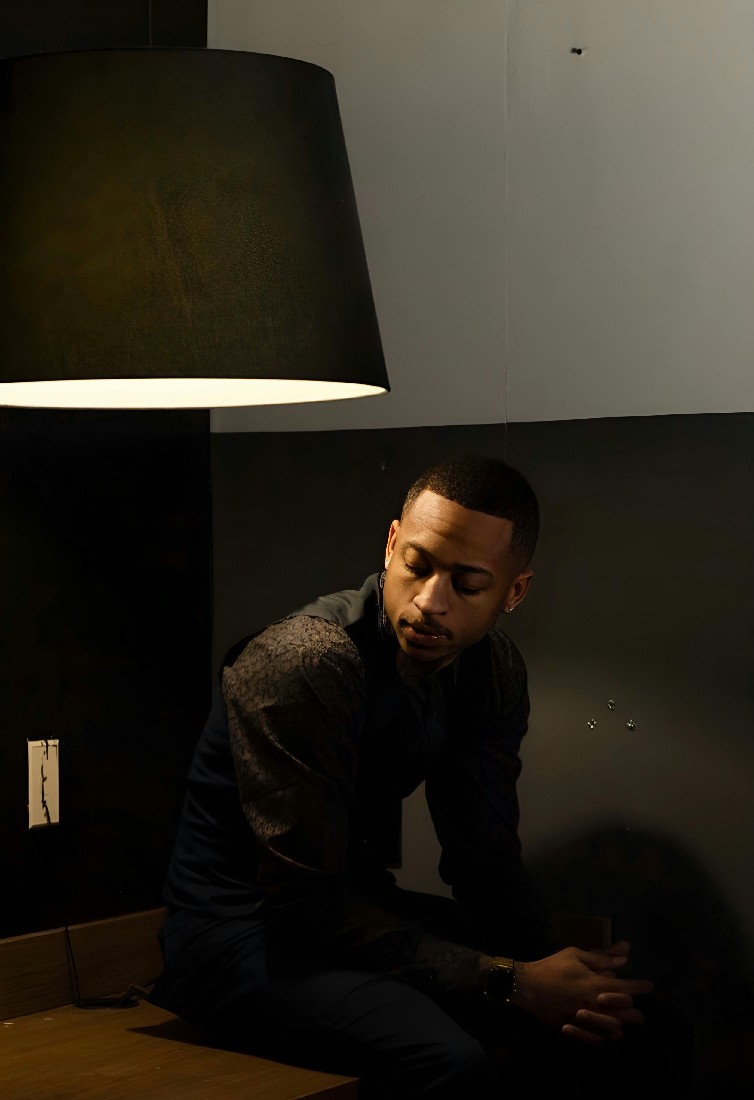 A stylish and thoughtful man sits under a modern lamp, exuding elegance in his attire.