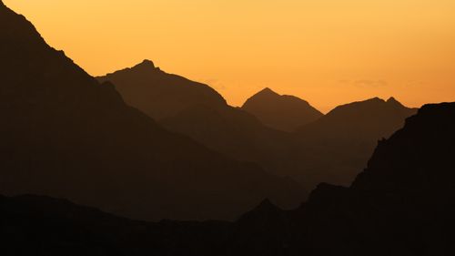 Free Silhouette of mountain peaks at sunset with a vibrant orange sky in the Alps. Stock Photo