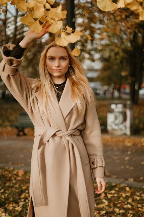 Free Fashionable woman in a beige coat posing in a leafy autumn park, embracing the fall season. Stock Photo