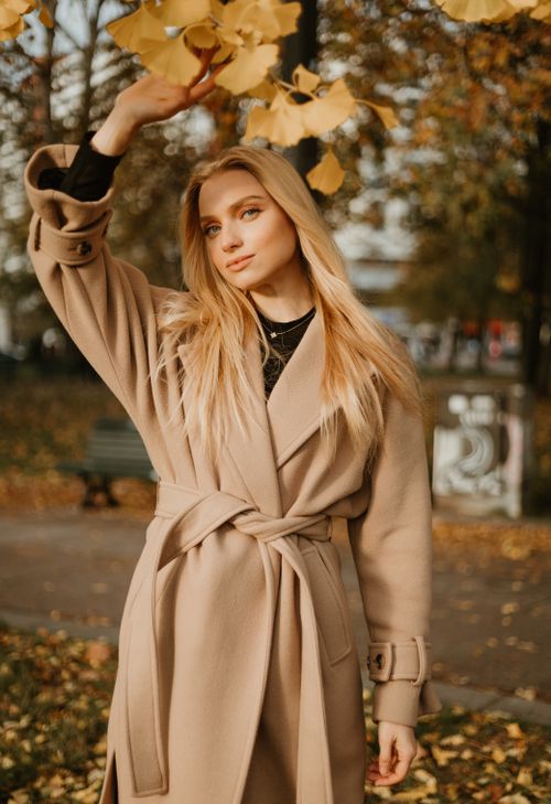 Free Stylish woman posing in a beige coat among autumn leaves in a park, showcasing fall fashion. Stock Photo