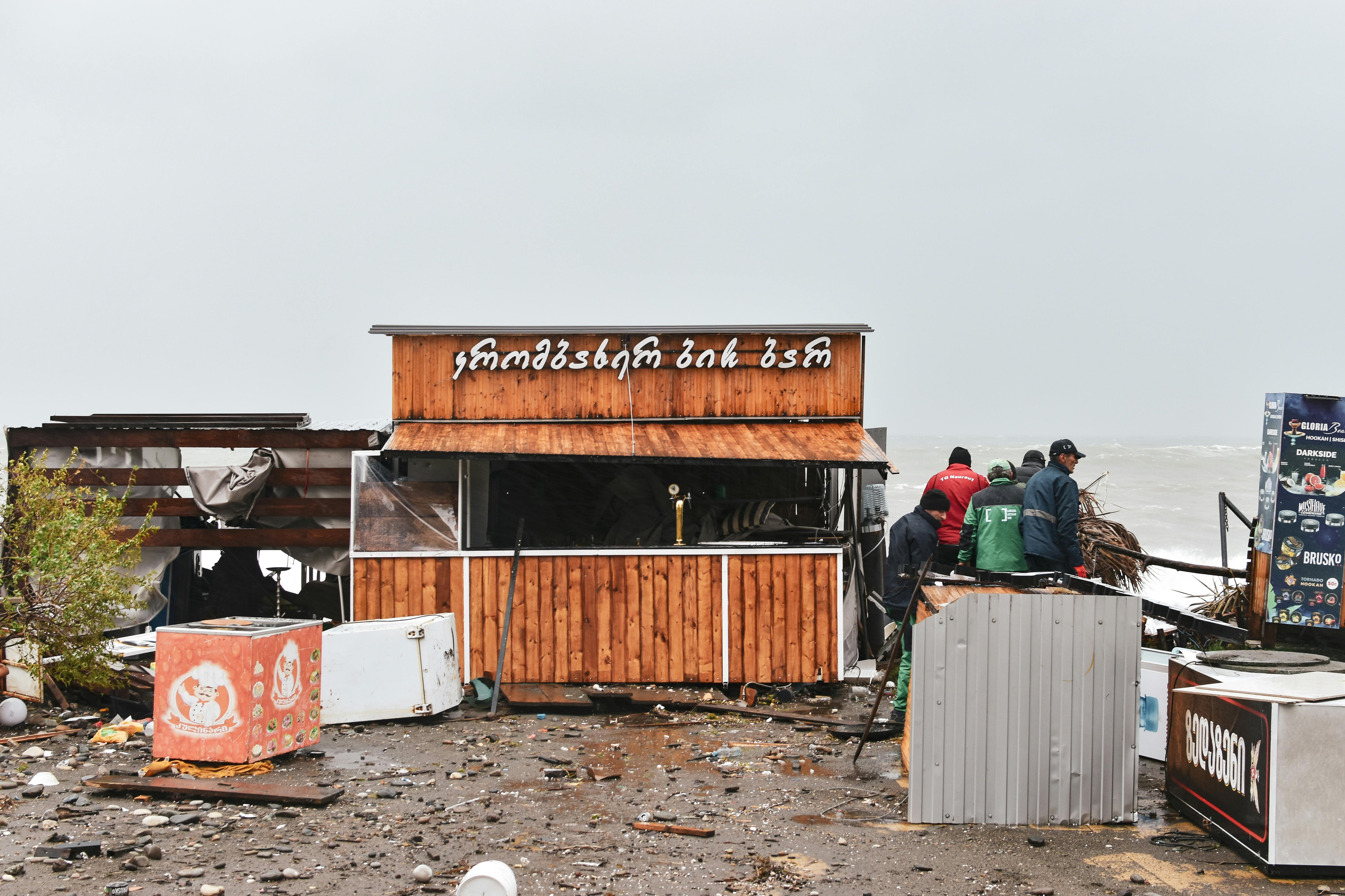 Street food stall shows storm damage by the coast, debris scattered around.