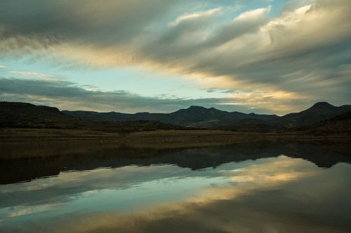 Free Calm lake reflecting mountains and dramatic sky during twilight, offering a serene landscape view. Stock Photo