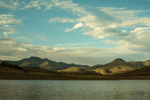 Free Peaceful landscape of a serene lake surrounded by rolling hills under a vivid sky. Stock Photo
