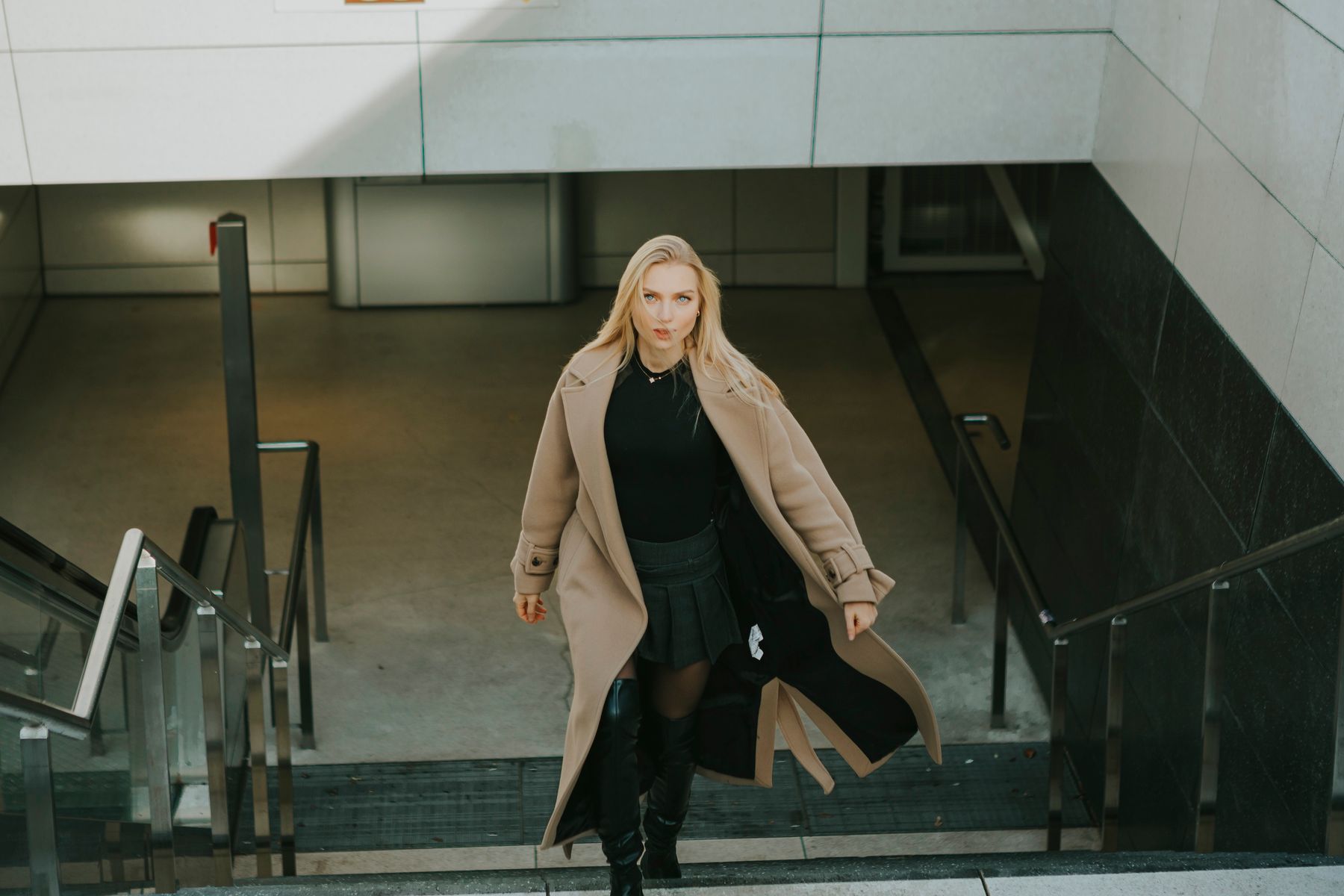Woman in a camel coat walking on architectural stairs