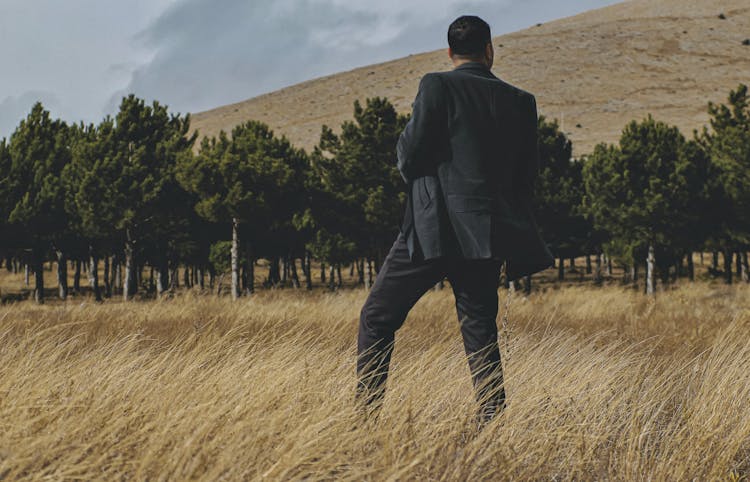 Back View Of A Man In A Suit Standing On A Grass Field 