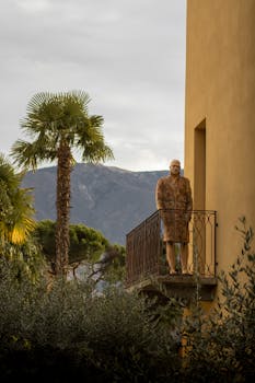 A mannequin stands on a balcony in Locarno, Switzerland, with a stunning mountain backdrop.