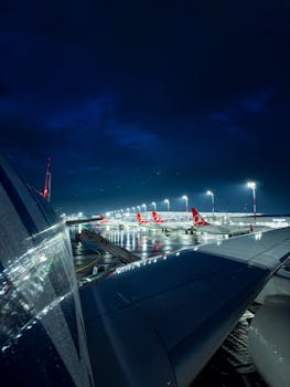 Illuminated airport with airplanes at night, view from aircraft wing.