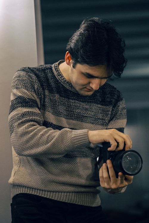 Free Adult male photographer inspecting camera, focusing indoors. Stock Photo