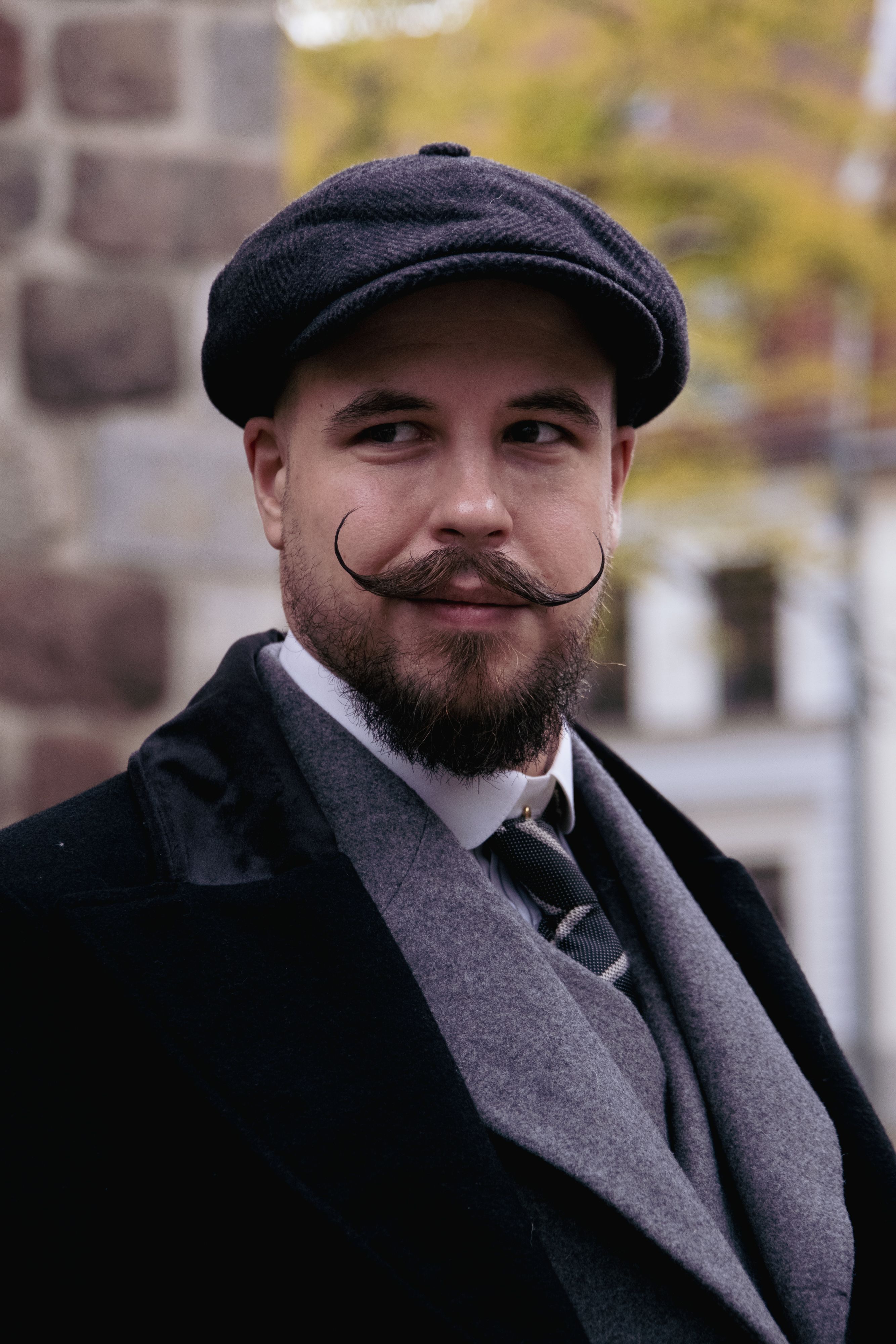 Stylish man with a mustache and beard in a suit and cap, outdoors in Berlin.