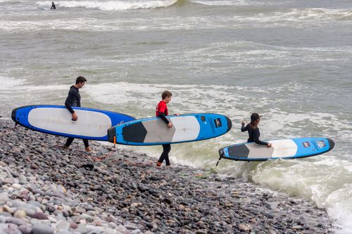 Free Three surfers with boards head into the ocean waves at Callao Beach, showcasing adventure and ocean lifestyle. Stock Photo