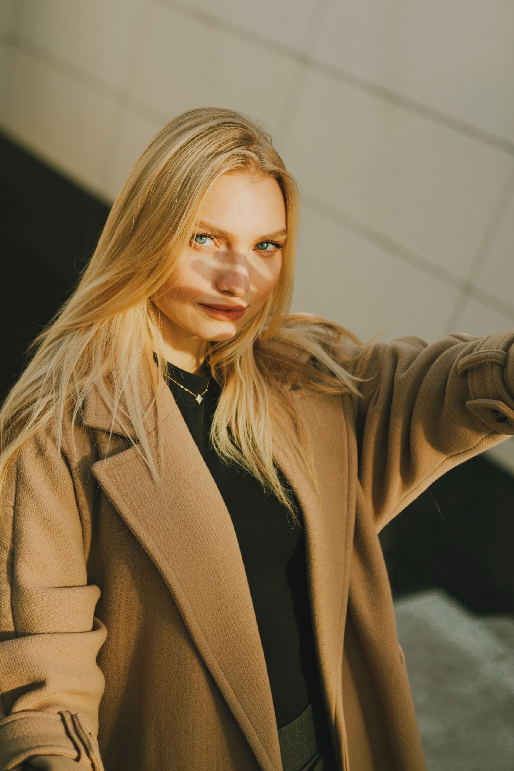 Blonde woman in a wool coat posing elegantly in an urban setting, showcasing fashion and sophistication.