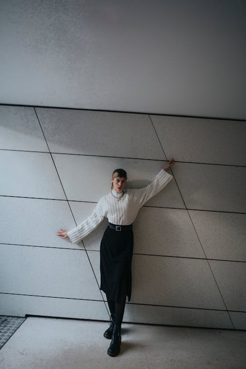 Young Woman in a White Turtleneck and Black Skirt Leaning against the Wall