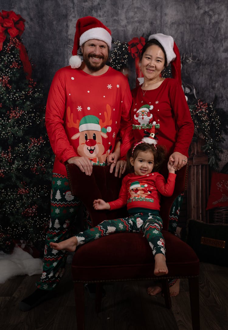 Family In Christmas Pajamas With Little Daughter Sitting On A Burgundy Velvet Chair