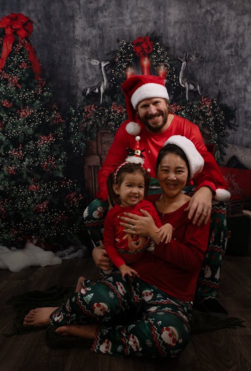 Parents and Daughter Posing under Christmas Tree in Red Christmas Pajamas