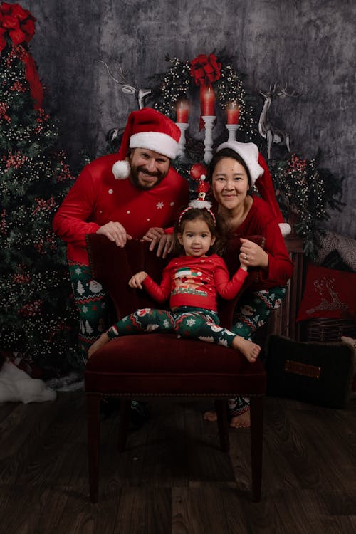 Couple with their Little Daughter Posing in Santa Hats in Front of a Christmas Tree 