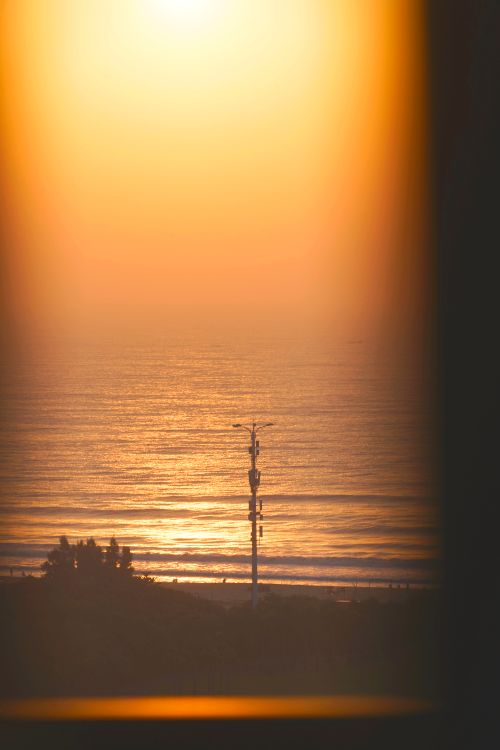 Free Captivating sunset view over the ocean, framed by a window, casting a golden glow. Stock Photo